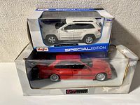 Photo of two model cars in their original boxes, including Maisto Special Edition Grand Cherokee Laredo and a red UT Models car.