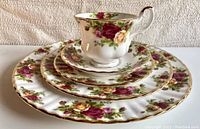 Side view of the five-piece place setting layered showing floral pattern and gold rim on each piece.