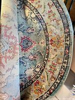 Photo showing folded edge of the round rug with visible multicolour pattern including turquoise, red, gold and other shades in floral design.