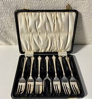 Front view of the set with six forks and one lifting fork inside an open satin-lined black case.