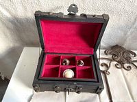 Open wooden treasure chest lined with red velvet showing four compartments containing costume rings