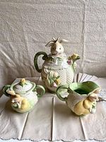 Three-piece vintage ceramic bunny tea set photographed on a cloth background, showing all key items.