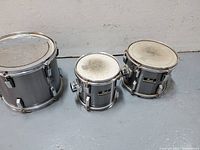 Photo of three silver Pearl tom drums arranged side by side against a white wall background.