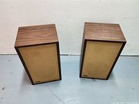 Front view of two speakers with wood veneer cabinets and tan cloth grills