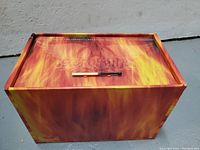 Closed fire-themed box set container with magnetic closure shown with matchstick for scale.