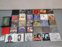 Top-down view of 24 CDs laid out on the floor with album covers clearly visible showing Metallica and Megadeth titles.