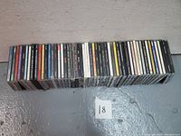 Top down view of all 36 music CDs in the lot stacked horizontally showing the spines with artist names and titles.