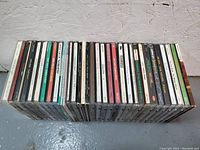 Top-down angled view of about 30 Sonic Youth CD cases lined up showing spines with album and single titles.