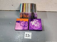 Stack of around 20 CDs including jewel cases and 2 mini box sets with purple photo covers showing children and band members.