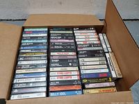Box of approximately 45 various popular 1980s music cassette tapes organized flat