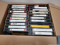 View of the box filled with VHS tapes stacked neatly showing handwritten and printed titles like Rush, KISS, and American History.