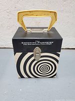 Photo of black and white spiral patterned metal box with yellow handle and latch closure, labeled 'The Smashing Pumpkins The Aeroplane Flies High'.