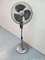 Full view of the Wind Chaser pedestal fan showing three black blades inside metal mesh cage and round weighted base with control panel.