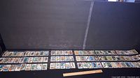 Wide view showing all trading cards laid out in rows on a flat surface with a black backdrop and a ruler for scale.