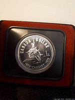 Front view of 1975 Canadian silver dollar coin in protective casing showing mounted rider design commemorating Calgary's centennial.