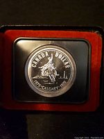 Close-up photo of the 1975 Canadian silver dollar coin commemorating Calgary, showing detailed coin design in protective display capsule.