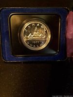 Close-up photo of the 1975 Canadian silver dollar coin housed in a clear protective case with blue velvet lining.
