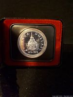 Close-up of 1976 Canadian silver dollar coin inside black case with red interior showing building design and text.