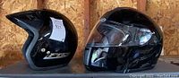 Side view of two black motorcycle helmets: Left open-face LS2 helmet, right full-face HJC IS-Max helmet