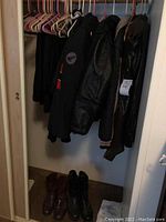 Photo of closet with four black jackets hanging and two pairs of boots on floor - one brown, one black