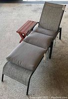 Full view of metal frame lounger with gray fabric and cushion, with small red wooden side table beside it