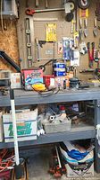 Full view of workshop shelf with various tools including chisels, car jack, cans, and sander