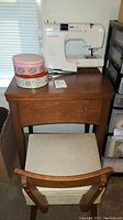 Photo of Singer sewing machine on wooden table with chair, decorative tins on table surface