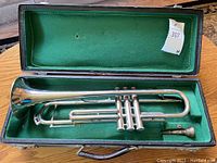 Silver-tone trumpet placed in an open green-lined black hard case, with mouthpiece beside it.