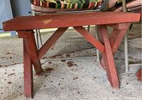 Close up of a painted wooden side table or footrest showing red paint with scratches and wear.