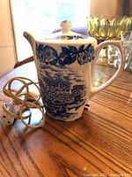Vintage electric tea pot ceramic with blue floral and scenic design on table, with electric cord visible.