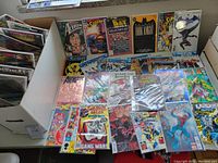 Photo showing various comic books including Superman, Batman, Spider-Man, Avengers, and Fantastic Four, some with foil, chrome and lenticular covers, arranged in a longbox and placed upright and flat.