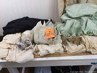 Wide view of assorted vintage textiles and clothing piled on table, showing mixed colors including dark and pastel tones.