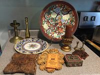 Photo showing entire item collection including plates, brass candlesticks, carved wooden panels, and decorative box on countertop.