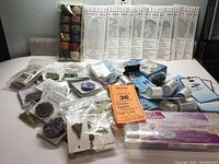 Lot contents including thread spools in multiple colors, assorted beads in bags and containers, needlecraft tools and accessories displayed on a table.