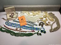 Overall lot showing a variety of blue, gold, pearl and green bead necklaces along with colorful pins and earrings