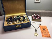 Overview of lot showing blue jewelry box with assorted jewelry, small box with beaded jewelry, and gold-tone zodiac necklace