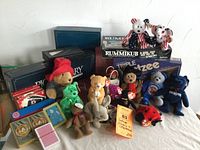 Photo showing collection of vintage board games and TY collectible bears arranged together. Games include Scrabble, Pictionary, Rummikub, Triple Yahtzee. Bears include 2004 Red Sox, Patriots, and other TY plush toys with tags.