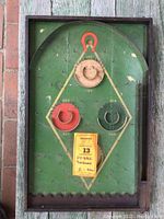 Front view of vintage Lindstrom Hy-Ball pinball game showing the green playfield with diamond scoring area, painted red, black and white target rings, and wooden frame with some wear and paint loss.