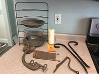 Overview showing metal pie rack with two trays, spool of twine, grater, clamps, hooks, and grinder on counter.