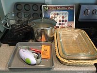Kitchen items displayed on countertop including Pyrex rectangular dishes in wicker holder, muffin pans, mixing bowl, Presto pressure cooker, and electric RoboTwist jar opener