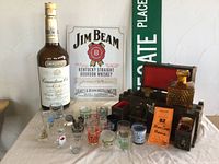 Full lot view showing mixed shot glasses, oversized Canadian Club bottle, Jim Beam and Tecate signs, and liquor decanter box with contents.