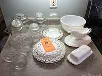 Photo showing milk glass bowls, plates, clear ribbed glass jars with lids, and covered butter dish arranged on a kitchen counter.