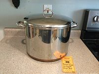 Full view of large stainless steel pot with copper bottom and lid on kitchen counter.