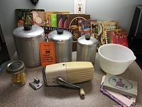 Overview of vintage kitchen items including cookbooks, canisters, ice crusher, mixing bowl, and small box