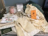 Overview of baby bonnets, cream knitted sweater, embroidered and lace table linens on table