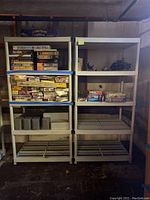 Two matching white plastic shelving units in basement with assorted boxed model kits and military miniatures on upper shelves. Shelves have a slatted design and some staining.