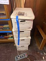 Stack of three white cardboard boxes with a blue tape strip visible on the top box and labels on the front.