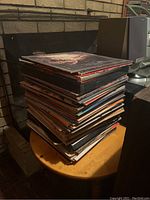 Stack of vinyl albums piled on a small round table next to audio equipment and speakers.