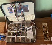 Open jewelry case showing assorted costume jewelry including beaded necklaces, bracelets, and rings in compartments.