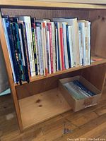 Photo of a wooden shelf holding the collection of modeling and military reference books neatly arranged vertically, some unidentifiable titles present.